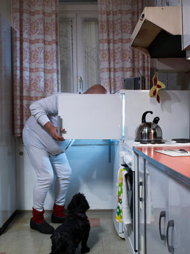 Man in nightwear and his dog looking into open refrigerator at night