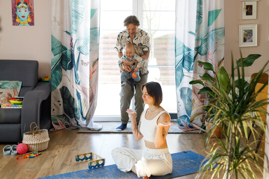 Mother meditating on yoga mat while father holds boy at home