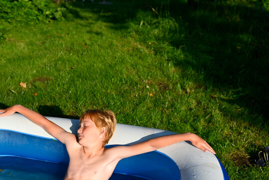 Red haired child relaxing in paddling pool in garden