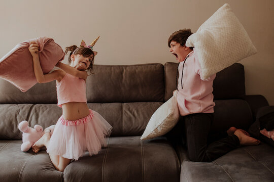 Playful siblings having a fun pillow fight on the sofa at home