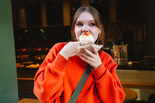 Customer in orange sweater eating a fruit pastry at a bakery