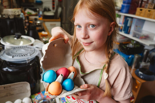 Girl holding carton of colorful Easter eggs in the kitchen