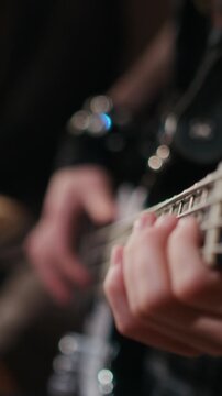 Vertical close-up shot of unknown musician playing bass guitar, fingers pressing strings on fretboard. Clip is ideal for music education promos or concert advertisements