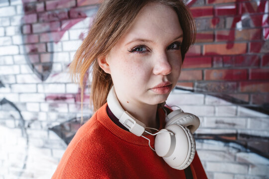Skeptical girl with headphone standing by graffiti wall outdoors