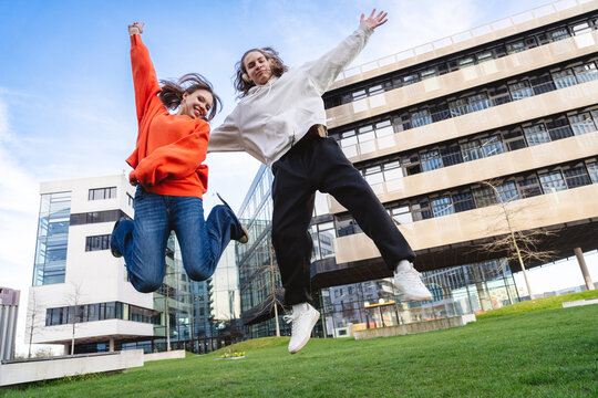Friends in casual clothing jumping with joy at city park