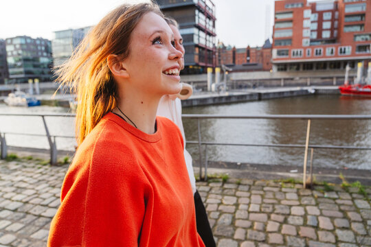Smiling girl in orange sweater walking outdoors by city river
