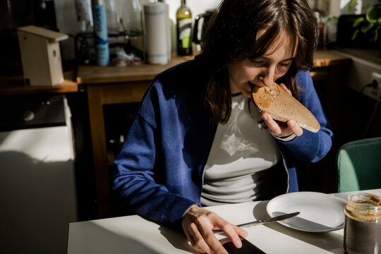 Young woman eating breakfast and looking at mobile phone