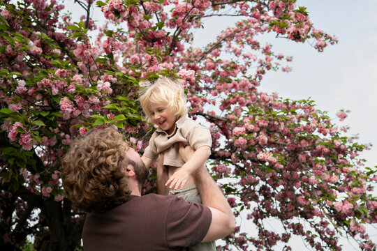 Smiling father lifting his son under a blooming spring tree