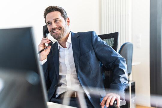 Smiling businessman talking on telephone at office desk
