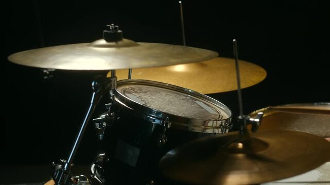 Energetic drummer playing powerful beat on drum kit with wooden sticks, hitting cymbals and toms during rehearsal or live performance in studio, dark background. Professional drummer playing on drums
