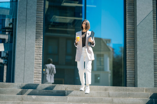 Businesswoman walking down office stairs with laptop and coffee