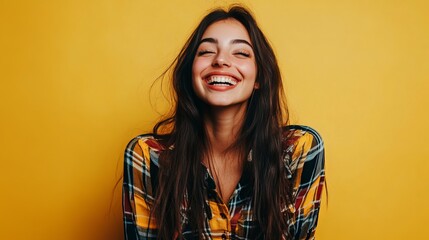 Fototapeta premium Happy young woman with long dark hair laughing joyfully against a vibrant solid yellow background