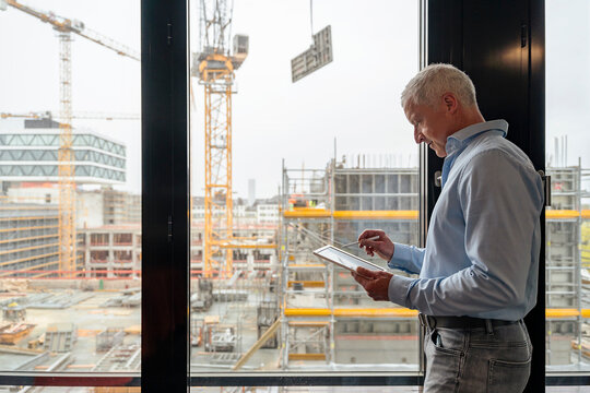 Architect with tablet at office window viewing construction site