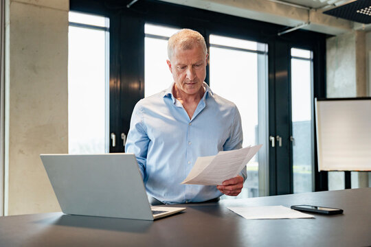 Executive reading business document at office desk in shirt