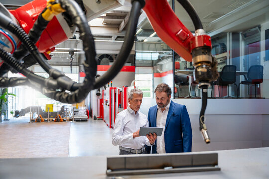 Manager and engineer using tablet near industrial robot