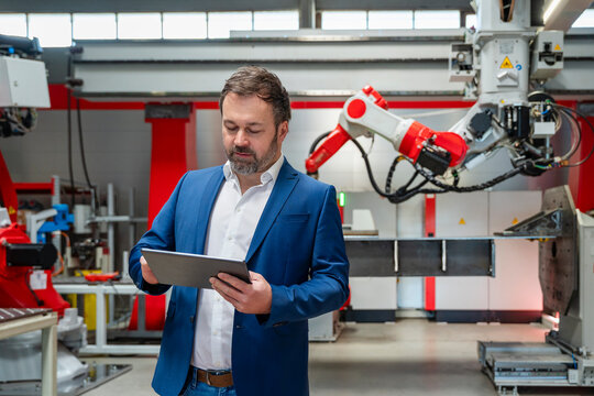 Manager using tablet in modern factory with industrial robot