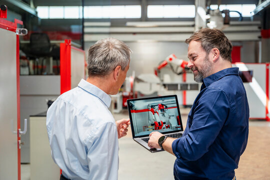 Engineers discussing industrial robot on laptop in factory