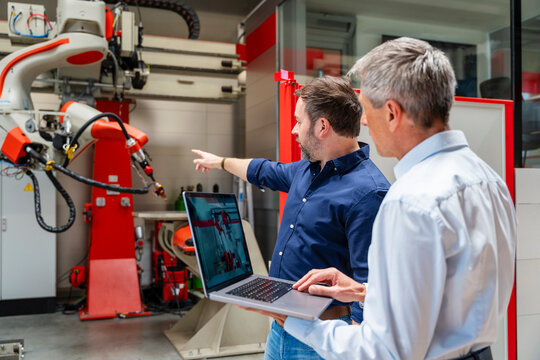 Employees planning automation with laptop and industrial robot