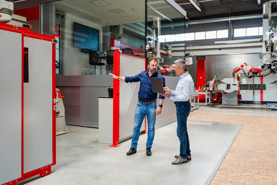 Engineers discussing production with laptop in modern factory