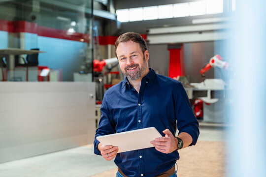 Smiling engineer holding tablet in modern automation factory