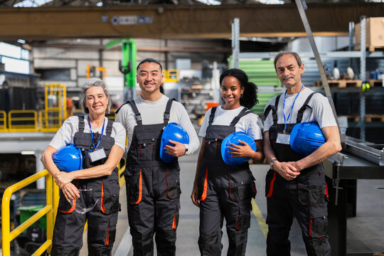 Smiling engineer and technician team holding hard hat in warehouse