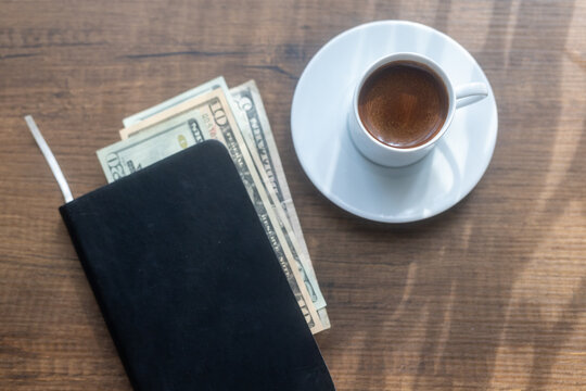Close-up of a cup of black coffee and cash money placed inside an open ledger notebook