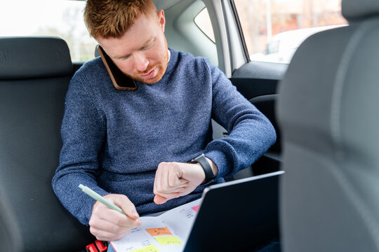 Businessman multitasking in a car with smartphone and planner