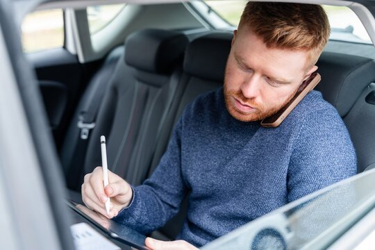 Commuter multitasking with phone and tablet in back seat of car