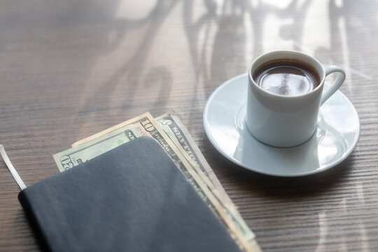 Close-up of a cup of black coffee and cash money placed inside an open ledger notebook
