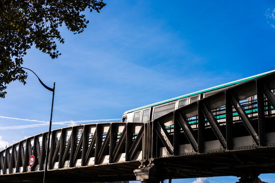 Paris metro runs across a bridge beneath blue sky, where elevated rail transport adds a strong urban line to the France city horizon