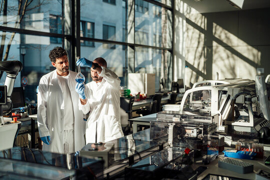 Scientists examining blue liquid in flask at bright laboratory