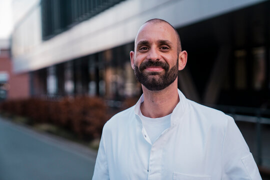 Smiling doctor in white coat standing outside a modern hospital