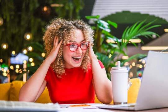 Excited architect in red working on laptop in biophilic workspace