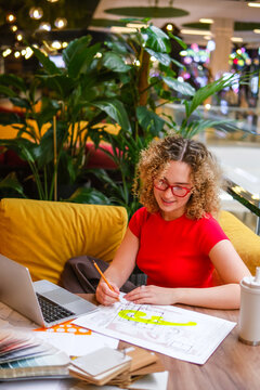 Smiling architect working on blueprint with laptop indoors