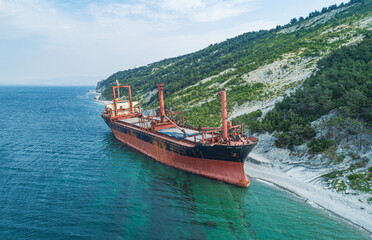 Fototapeta premium Grounded derelict cargo ship on a rocky Black Sea beach with green mountains under a bright sky