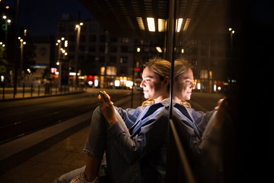 Woman using mobile device at urban station at night