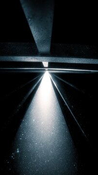 Dramatic beam of bright light piercing through metal structures illuminating floating dust particles in a dark industrial environment creating a mysterious atmospher