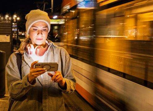 Woman texting on mobile phone at night with tram in background