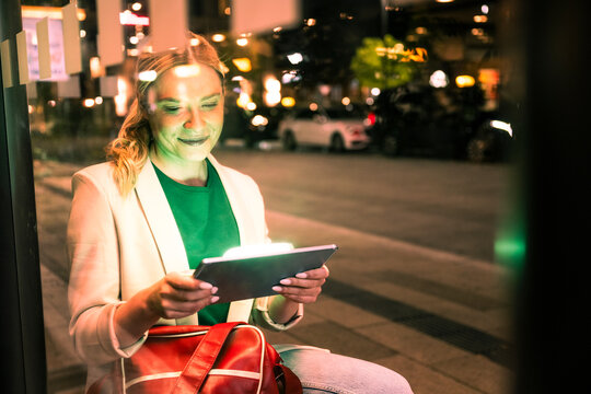 Woman using digital tablet at city bus stop at night