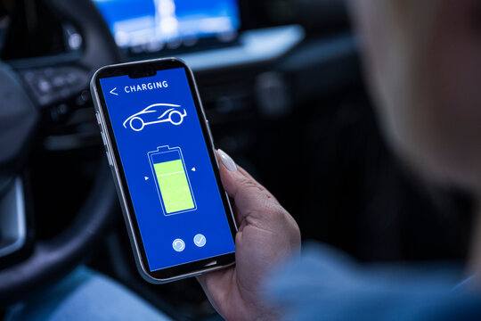 Hand holding smartphone with charging app inside electric car