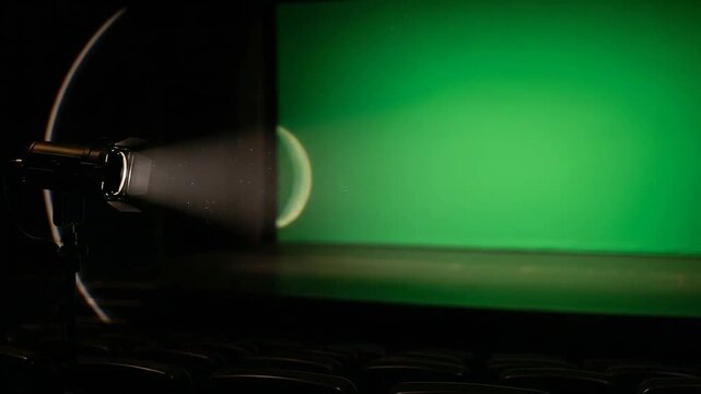 A bright spotlight illuminates a large green screen in a dark empty theater room