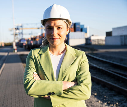 Smiling logistics manager in hardhat standing at outdoor freight port