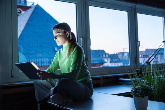 Concentrating woman working on tablet in dark office at night