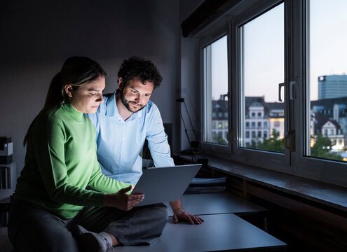 Colleagues working at night on laptop in dark office