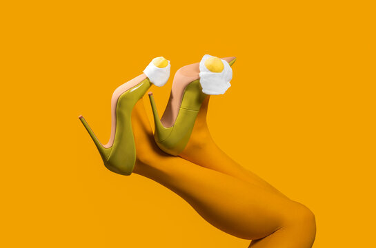Surreal legs in green heels with eggs on top against yellow background
