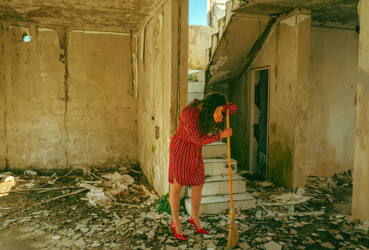 Exhausted cleaner resting on broom in a ruined building