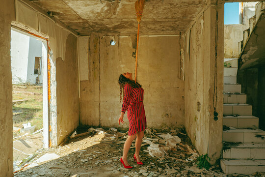 Woman balancing a broom in ruined room as burnout metaphor