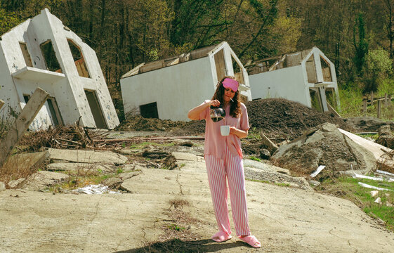 Woman in pajamas pouring coffee and smoking amidst destruction