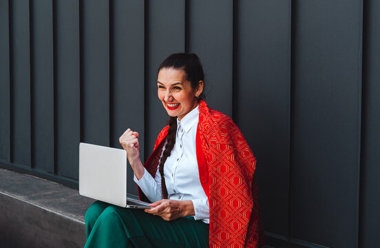 Cheering freelancer holding laptop outdoors celebrating success
