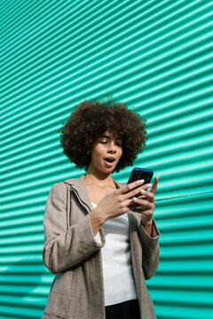 Surprised womanreading message on smartphone against turquoise wall
